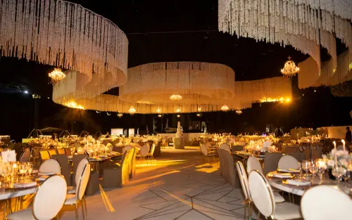 Salón de eventos decorado con estructuras colgantes florales, candelabros y mesas elegantemente dispuestas para un banquete de lujo.