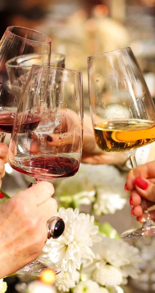 Brindis con copas de vino tinto y blanco, celebrando en un evento social con decoración floral de fondo.