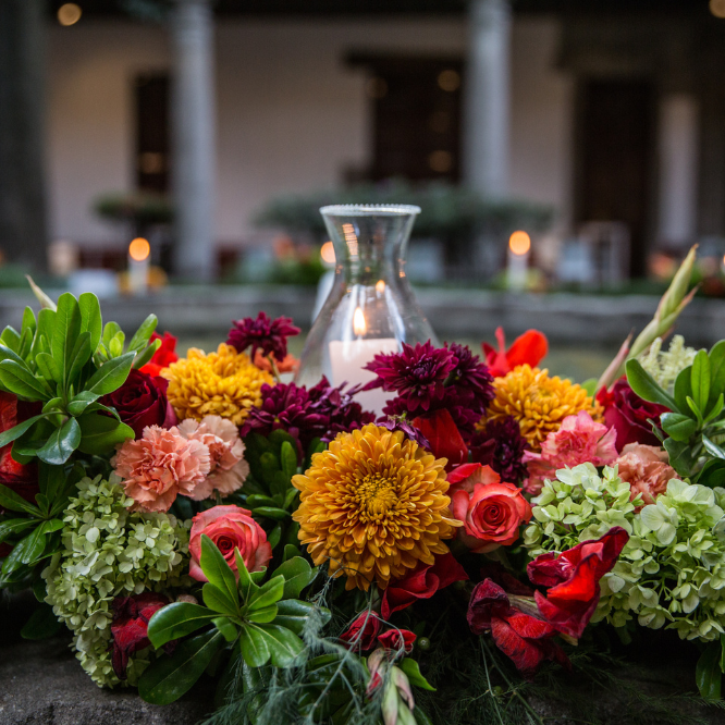 Arreglo floral colorido con rosas, crisantemos y follaje, decorando un centro de mesa elegante.